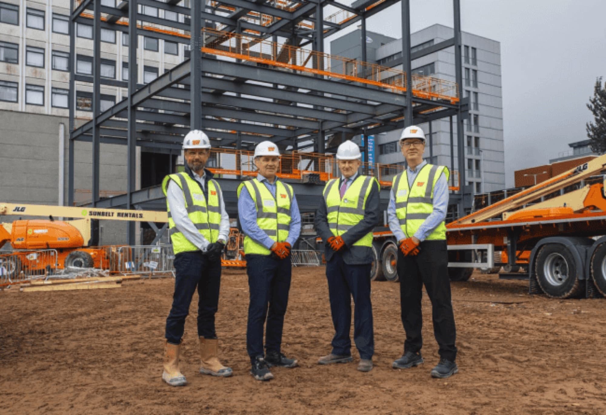 Four Eric Wright colleagues in hard hats and hi-vis on site in front of a new steel frame